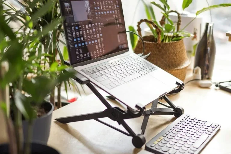 Laptop auf Schreibtisch mit externem Keyboard und Pflanzen im Hintergrund